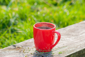 A red cup of aromatic coffee on a wooden bench, outdoors. Sunny morning