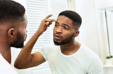 Young worried african man checking his wrinkles