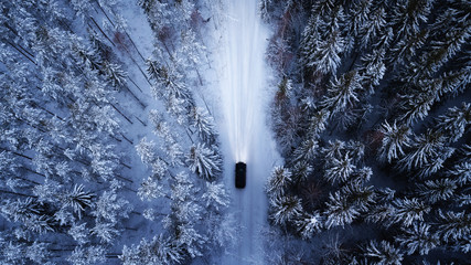 Aerial view of a car on winter road in the forest.  Aerial photography of snowy forest with car on the road.  Aerial photo. Car in motion