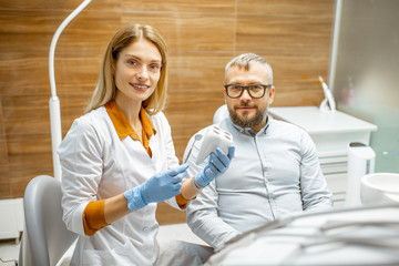 Obraz premium Portrait of a female dentist with tooth model and handsome man as a patient during a medical consultation at the dental office