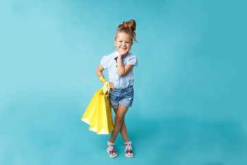 Little cute and funny girl holding big bright colored yellow paper bags in the blue studio