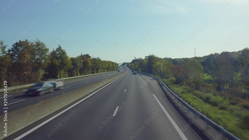 Poster fly over a highway covered with the greenery including trees and green fields, passing the fast driv