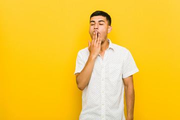 Young hispanic man yawning showing a tired gesture covering mouth with hand.