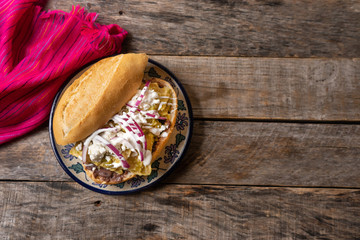 Mexican green chilaquiles sandwich with cheese also called "guajolota" or "torta de chilaquiles" on wooden background