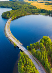 Landscape of an asphalt road. View from above on the road going along the blue lake, fields and forest. Paijanne National Park, Finland.