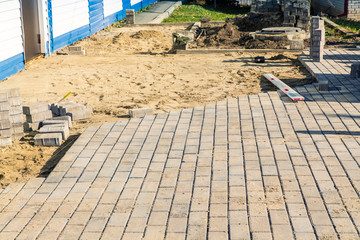 Laying gray concrete paving slabs on leveled yellow sand