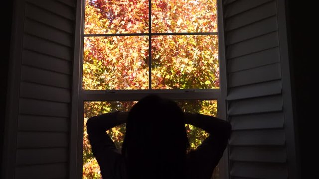 4K autumn stock footage video. An unidentifiable woman looks out the window as she ties her hair up in a bun and does a few yoga stretches to start her day.