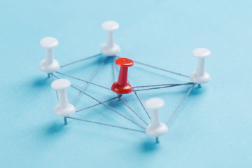 network with red and white pins and string, An arrangement of colorful pins linked together with string on a blue background suggesting a network of connections.