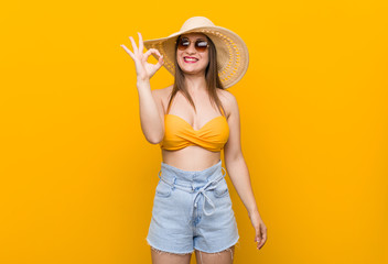 Young caucasian woman wearing a straw hat, summer look cheerful and confident showing ok gesture.
