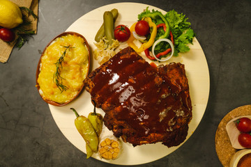 Roasted pork ribs BBQ with baked potato and salad on wooden plate