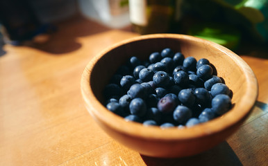 A bowl of ripe fresh blueberries in a rustic wooden bowl in the sun with copy space to the left.