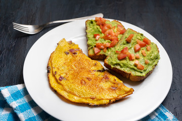 Healthy breakfast with omelette and guacamole toast on dark background