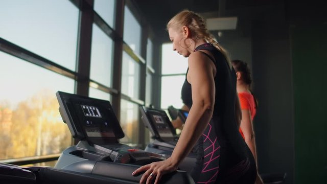 A woman walks up to the treadmill and turns it on to start training. Include a treadmill in the gym fitness room