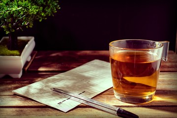 cup of hot tea, postal envelope, bonsai and pen on a wooden surface