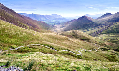 Three distant hikers walking up a winding rocky path from Coledale Beck that leads to Hopegill...