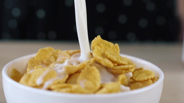 Milk is poured into a bowl with cornflakes in slowmotion. Dry breakfast sereals. Food close up.