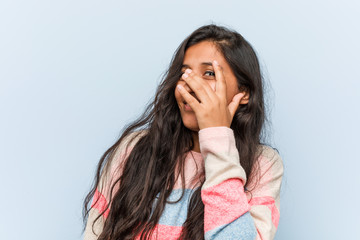 Young fashion indian woman blink at the camera through fingers, embarrassed covering face.