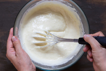 Top view of woman hand mixing with whisk dry ingredients and batter on wooden background
