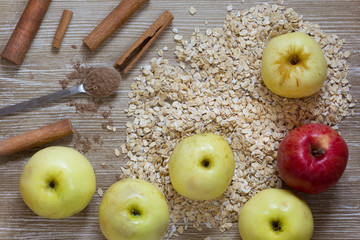 Top view of apples, oats, cinnamon sticks as ingredients for baked apples on wooden background
