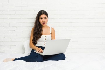 Young arab woman working with her laptop on the bed screaming very angry and aggressive.