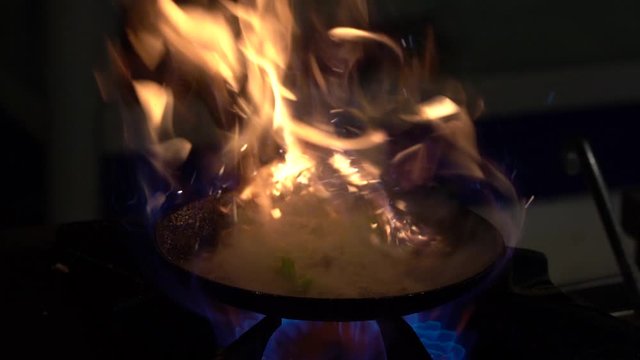 Chef frying vegetables on fire throwing them in a frying pan. Slow motion view of frying pans with vegetables on big fire flame at street cafe in Turkey. Cook frying vegetable in the kitchen