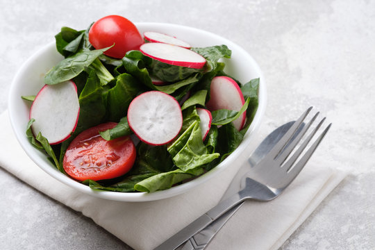 Fresh spring salad with green leaves of arugula, , spinach, beets, radish, cucumber and tomato on a gray stone background.