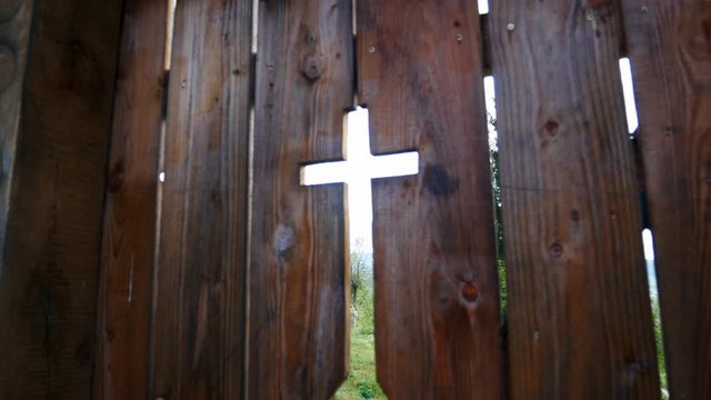 Old wooden gate with a cross shaped hole that gives entrance to a cemetery and church