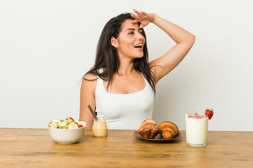 Obraz na płótnie Canvas Young curvy woman taking a breakfast looking far away keeping hand on forehead.