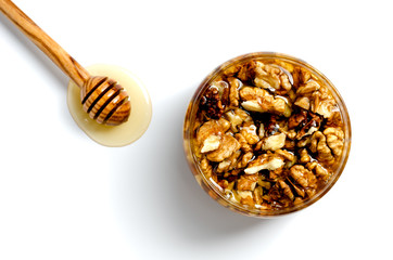 Tasty walnut with honey in a glass jar on a white isolated background. Nearby lies a spoon with...