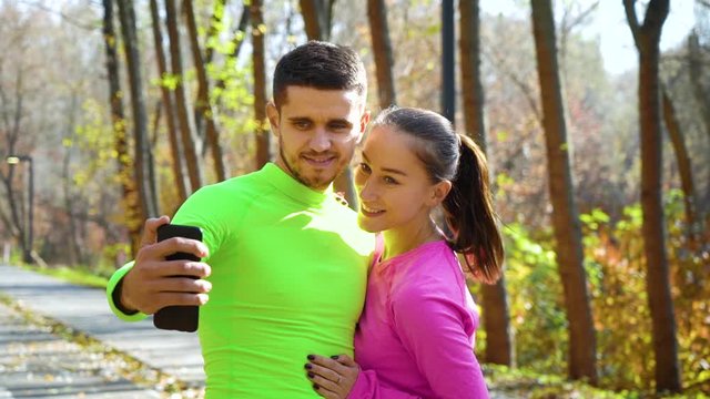 Smiling athletic couple in sportswear taking selfie photo in autumn park