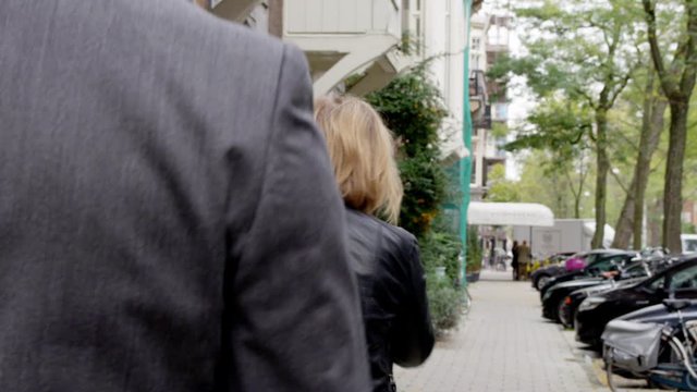 Man stalker following woman too close in city. Suspicious movement. Unregognizable shots from back. Bicycles and cars parked at right side. Slowmotion.