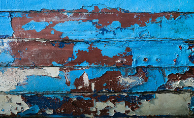 Worn and peeling paint on a wooden boat in blue & red.
