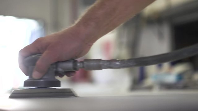 Man using a sander to smooth out a large metal sheet. View from the inside of a workshop. Slow Motion.