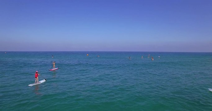 Drone shot flying over a dozens of people paddling out on Stand-Up paddle boards for a public event off of the coast of Tel Aviv Beach, Israel. 