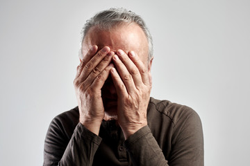 Portrait of senior citizen man covered his face with hands isolated on a white background