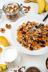 Granola muesli breakfast with with milk, dried apricots, cranberries, almonds and flax seeds in bowl on a white background. Healthy cereal breakfast.