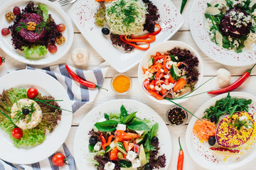 Festive banquet table. Top view of vegetable salads assortment on white wooden background.