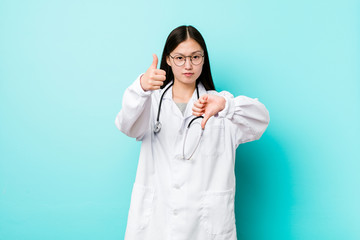 Young chinese doctor woman showing thumbs up and thumbs down, difficult choose concept