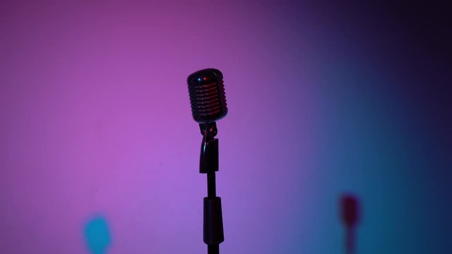 Professional concert vintage glare microphone for record or speak to audience on stage in dark empty retro club close up. Spotlights shine on a chrome mic in the middle on lilac blue color background.