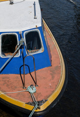 View of an old boat moored at a dock from above in white, blue & orange with dark water.