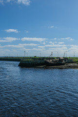 Obraz premium View of the River Corrib flowing into Galway Bay, Ireland & the old boats & wrecks on a sunny summer day with blue sky. Taken in the city.