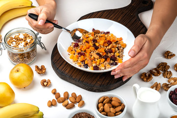 Woman eating breakfast bowl of granola muesli with milk, dried apricots, cranberries, almonds and flax seeds. Female hands hold healthy natural detox food.