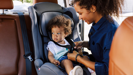 Little boy sitting in a baby seat looking away while mother fastening him  - Powered by Adobe