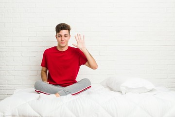 Young teenager student man on the bed smiling cheerful showing number five with fingers.