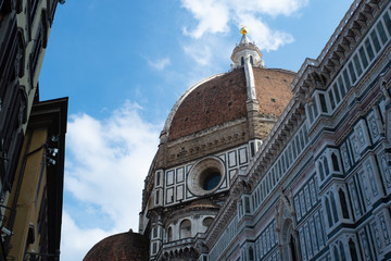 Florence's Santa Maria del Fiore Dome seen from the side with clouds and blue sky.
