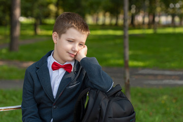 Portrait of a thoughtful 10 years old boy in a school jacket with a red bow tie and backpack.