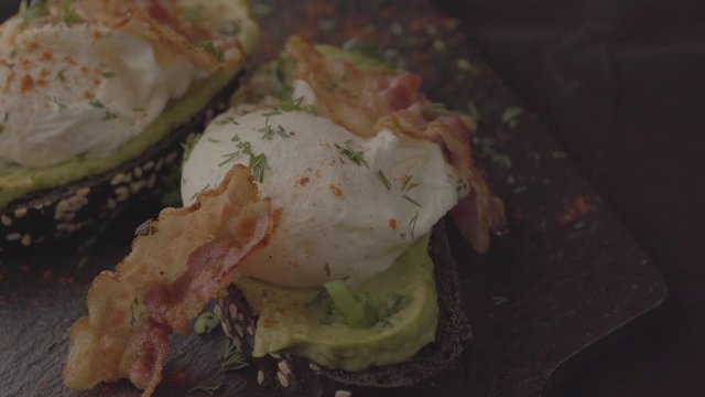 Poached eggs with bacon on toasts. Laid out on black slate.