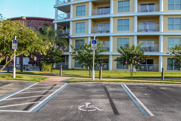 Two signs with the wheelchair logo stating: "Parking only for disabled people". The strips marked on the pavement in blue and white. In the background a beautiful building in cream and white colors.