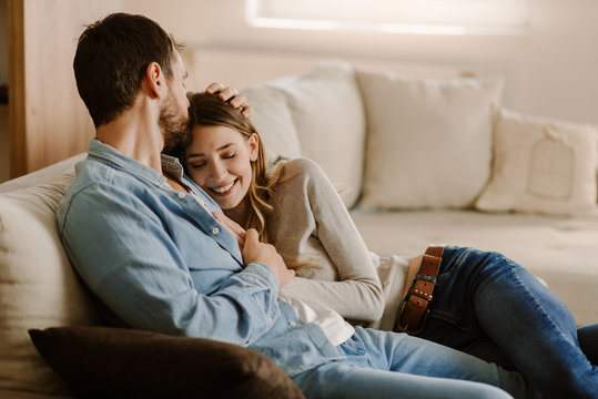 Smiling woman enjoying at home while her boyfriend is kissing her in the head