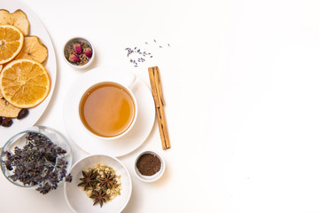 a white mug on a white table with herbal tea and herbal ingredients laid out on the table. Concept on the topic of herbal treatment for colds and flu in autumn. Top view